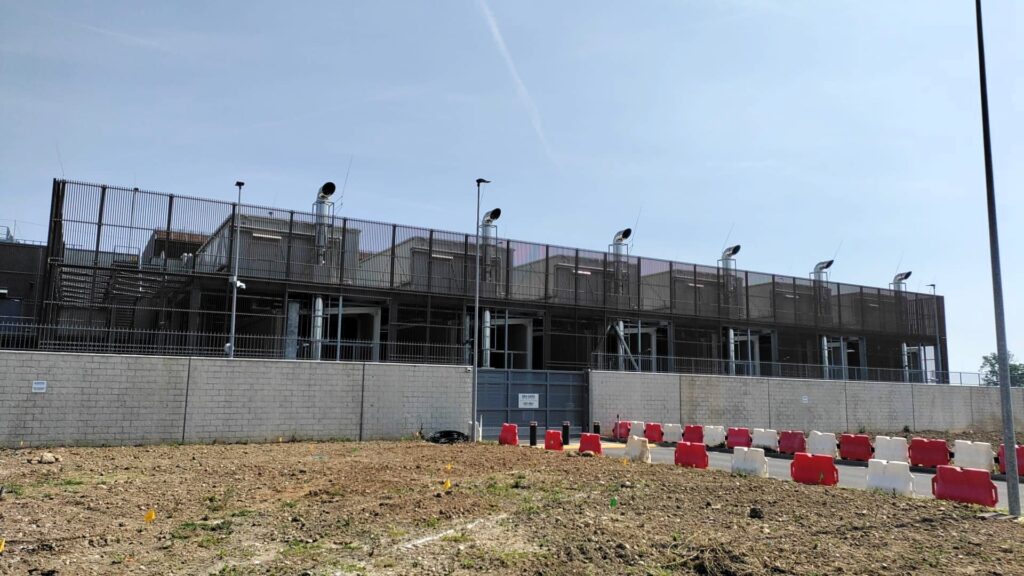 A row of large diesel backup generators with exhaust stacks behind a security fence at a data center under construction