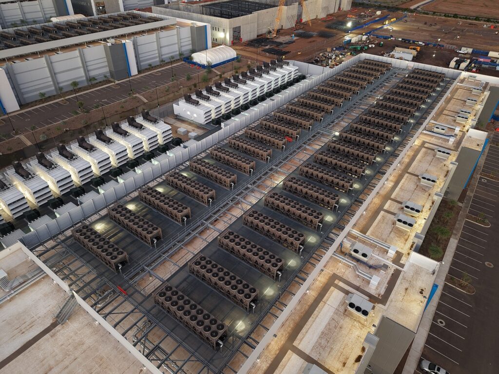 Aerial view of a data center roof lined with rows of fan-cooled cooling units, with backup generators along one side